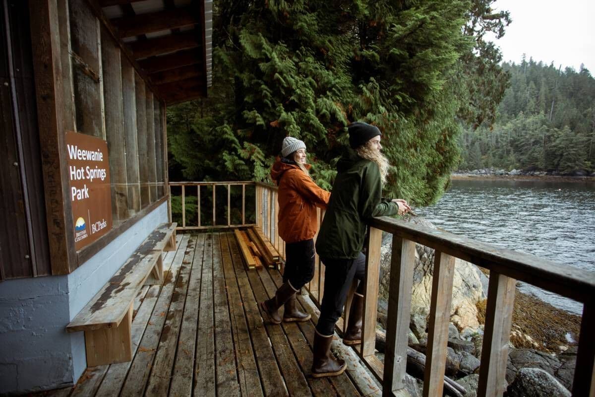 Visitors pause on the wooden deck at Weewanie Hot Springs Park, soaking in the tranquil waterfront views and the peaceful ambiance of the surrounding nature.